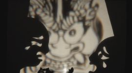 a imagem apresenta a preto, num primeiro plano, 3 figuras com traços humanos a gritarem e em fundo claro, iluminado a branco, um desenho em sombra de uma figura monstruosa ao estilo japonês